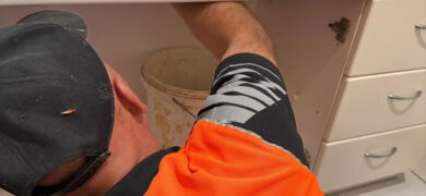 Plumbing Problems being repaired by a GoFox plumber fixing pipework under a bathroom vanity during a professional maintenance job.