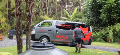 Finding the Right Plumber with a GoFox technician walking toward a branded plumbing van beside a rural water tank surrounded by native bush