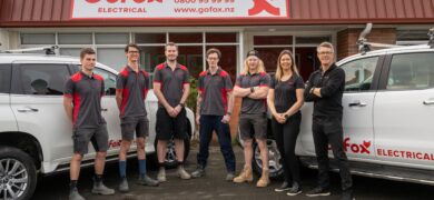 Join a Franchise with GoFox team standing together outside their electrical branch, with branded vehicles parked on each side.
