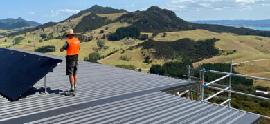 Solar Power Solutions rooftop installation by GoFox Electrical Whangarei technician fitting solar panels on rural Northland property with rolling hills in the background