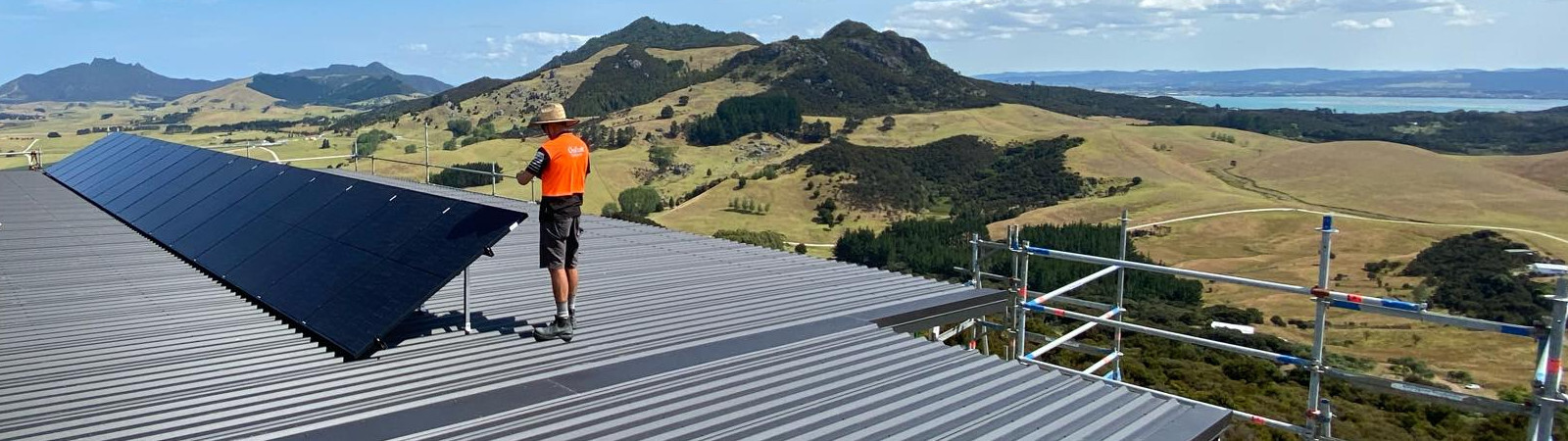 Solar Power Solutions rooftop installation by GoFox Electrical Whangarei technician fitting solar panels on rural Northland property with rolling hills in the background