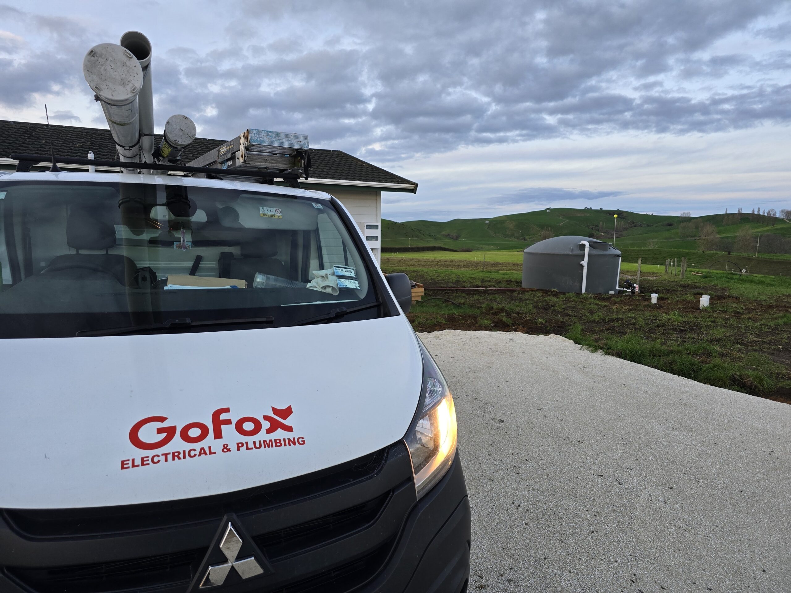 Preventative Plumbing Maintenance with a GoFox Electrical & Plumbing van parked on a rural property near water system equipment and rolling green hills
