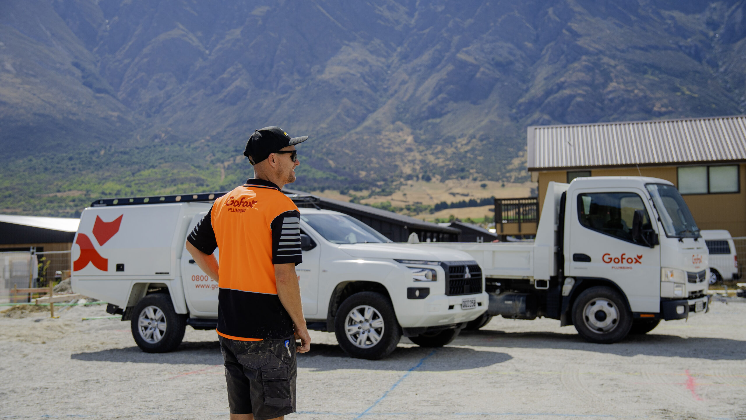 Trades Businesses Hit a Growth Ceiling showing a GoFox worker standing beside branded service vehicles at a regional worksite with mountains in the background
