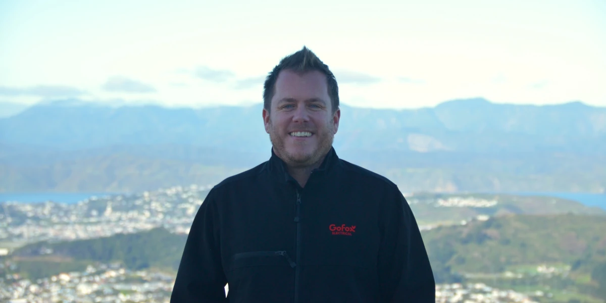 GoFox Electrical owner Dan McLaughlan standing at a scenic Wellington lookout with city and harbour in the background