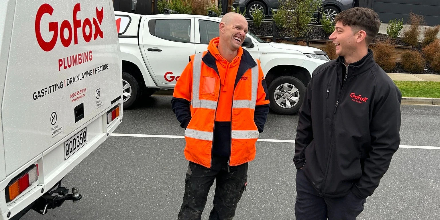 Electrical and Plumbing Franchising NZ showing GoFox Electrical and GoFox Plumbing franchise owners chatting beside branded service vehicles on site