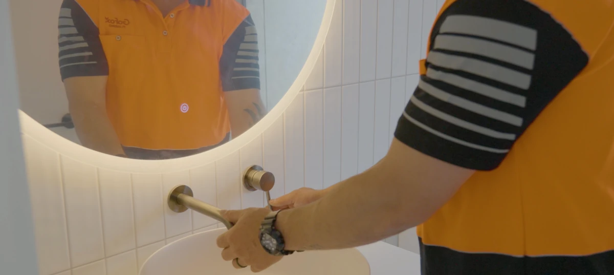 Kitchen Plumbing Upgrades showing a GoFox plumber installing a modern wall mounted tap beneath a round LED mirror in a tiled bathroom vanity