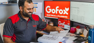 Is a franchise worth the cost – GoFox electrical and plumbing team member reviewing plans at desk with branded screens in the background