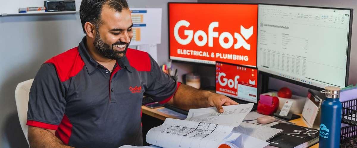 Is a franchise worth the cost – GoFox electrical and plumbing team member reviewing plans at desk with branded screens in the background