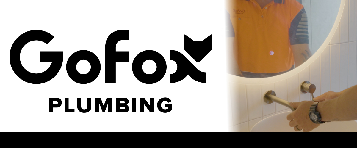 Renovation plumbing work in progress, GoFox Plumber in orange polo shirt installing bath tapware in a white tiled bathroom, reflected in a round mirror